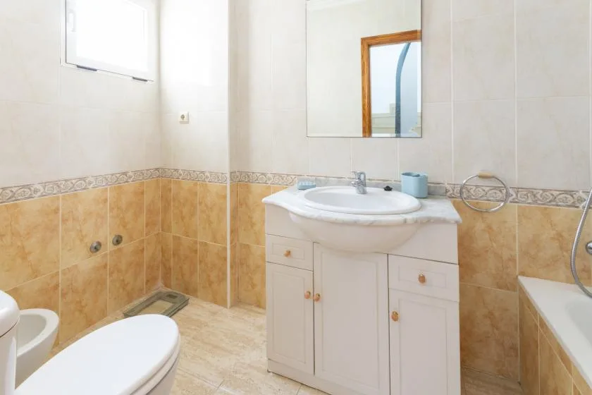 A tiled bathroom with a sink vanity, mirror, toilet, and bathtub.