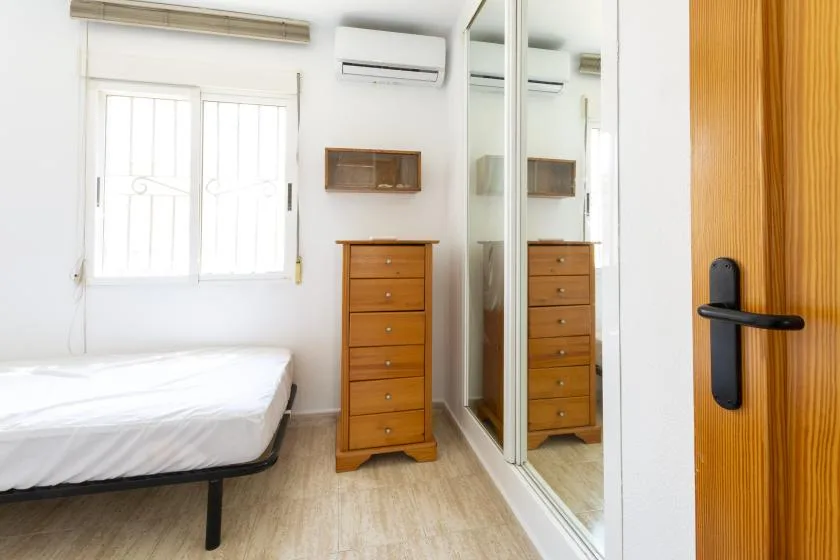 A bright bedroom with a bed, wooden dresser, and mirrored wardrobe.
