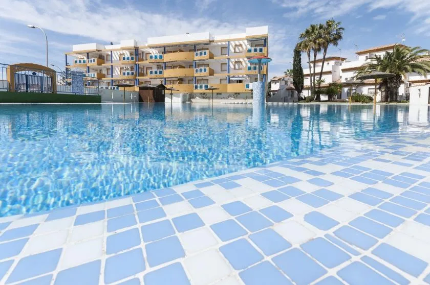 An outdoor swimming pool with blue-and-white tiled decking and apartment buildings in the background.