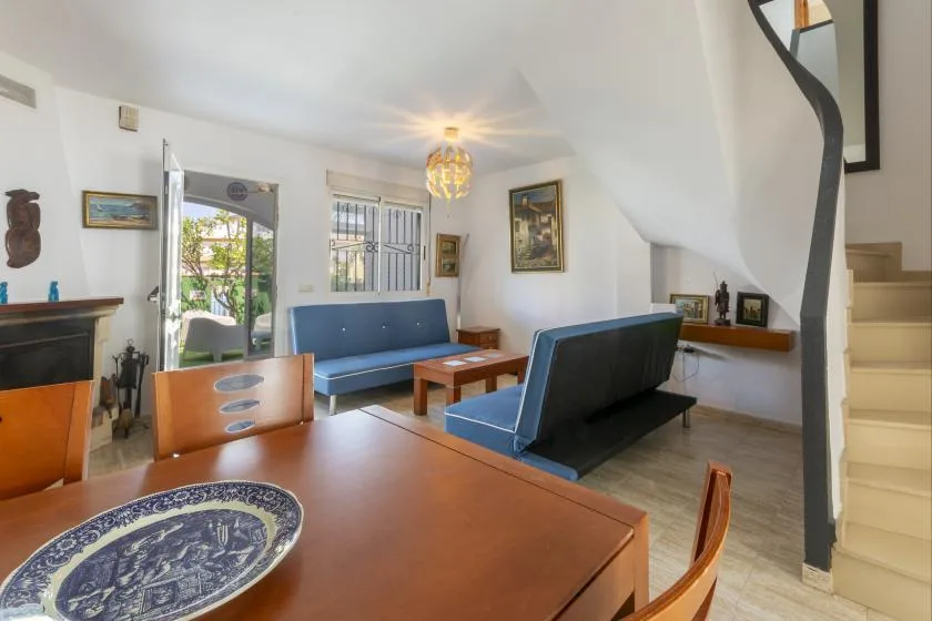 A living room with blue seating, a wooden table, and a staircase.