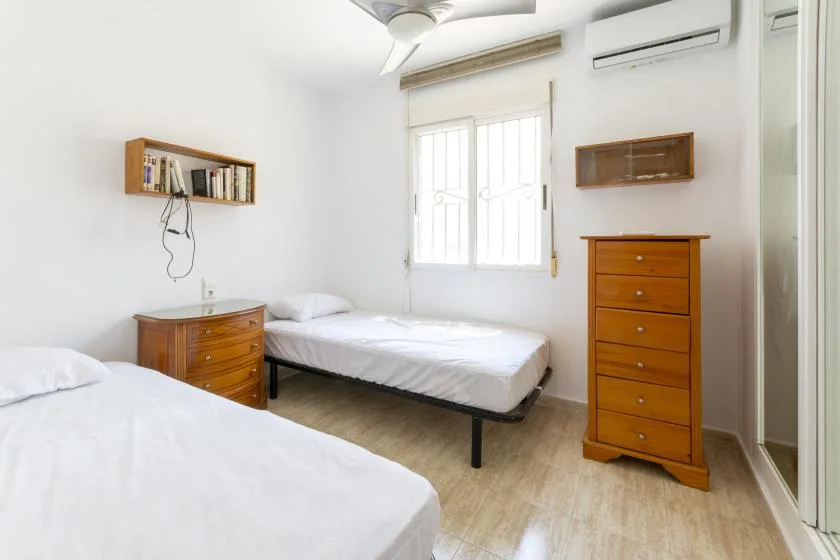 A bright bedroom with two beds and wooden dressers.