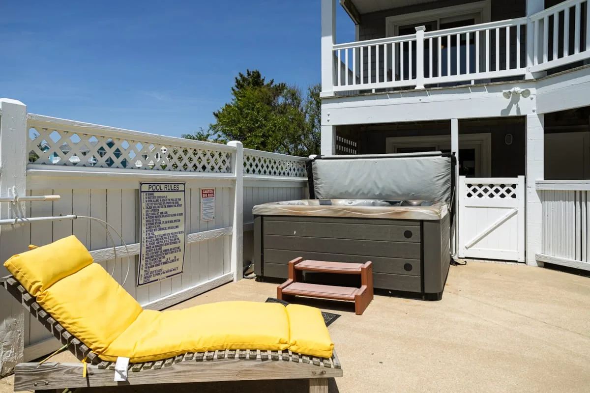 A sunny outdoor patio with a yellow lounge chair and a covered hot tub.