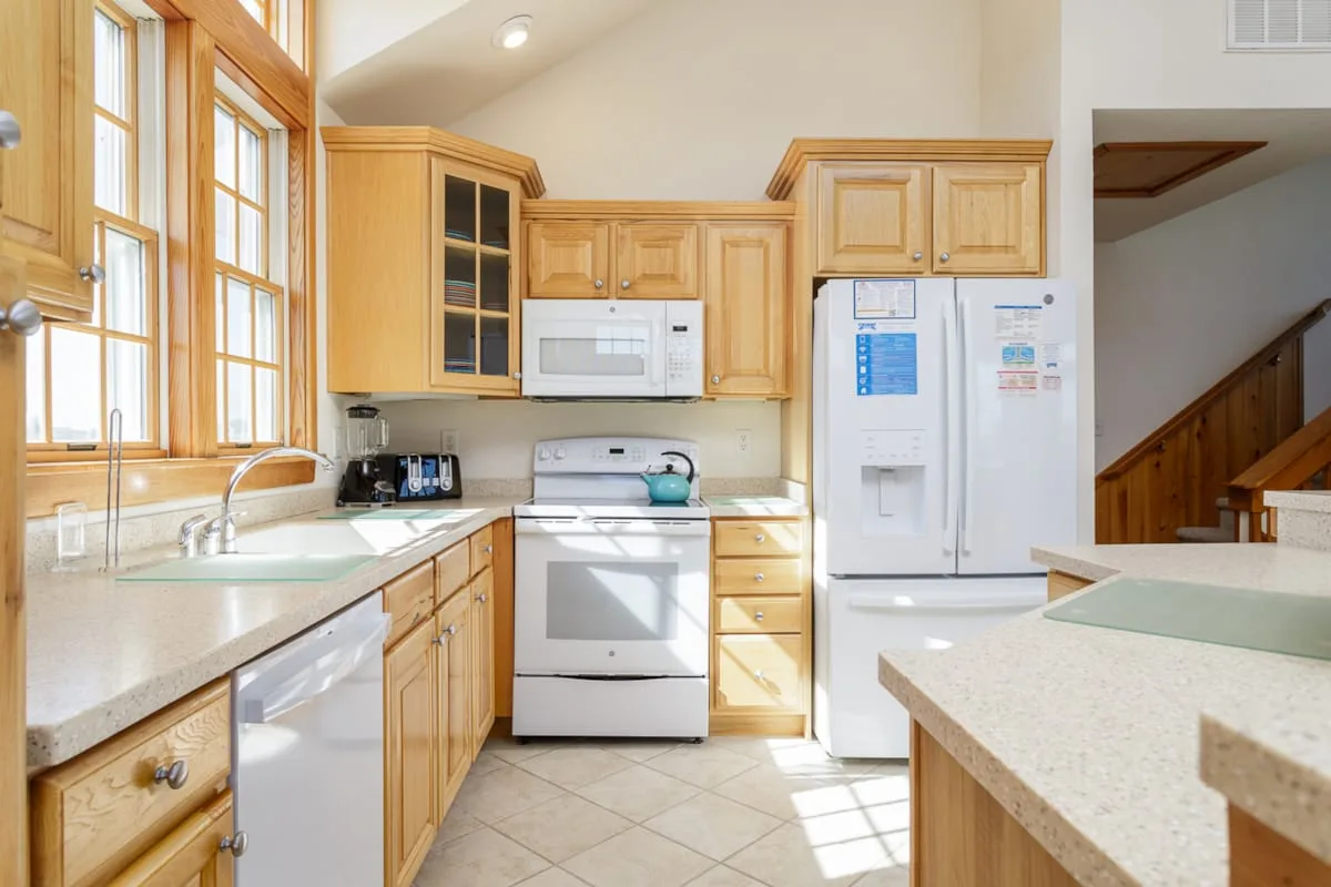 A bright kitchen with light wood cabinets, a sink, and a central cooking area.