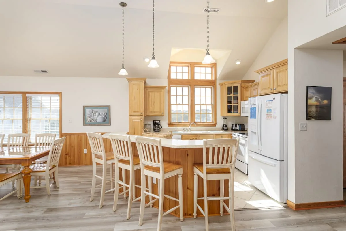 A bright open kitchen and dining area with a central island and large windows.