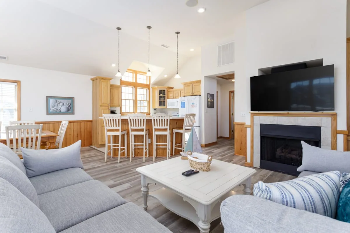 A bright open-plan living and dining area with a television above the fireplace.