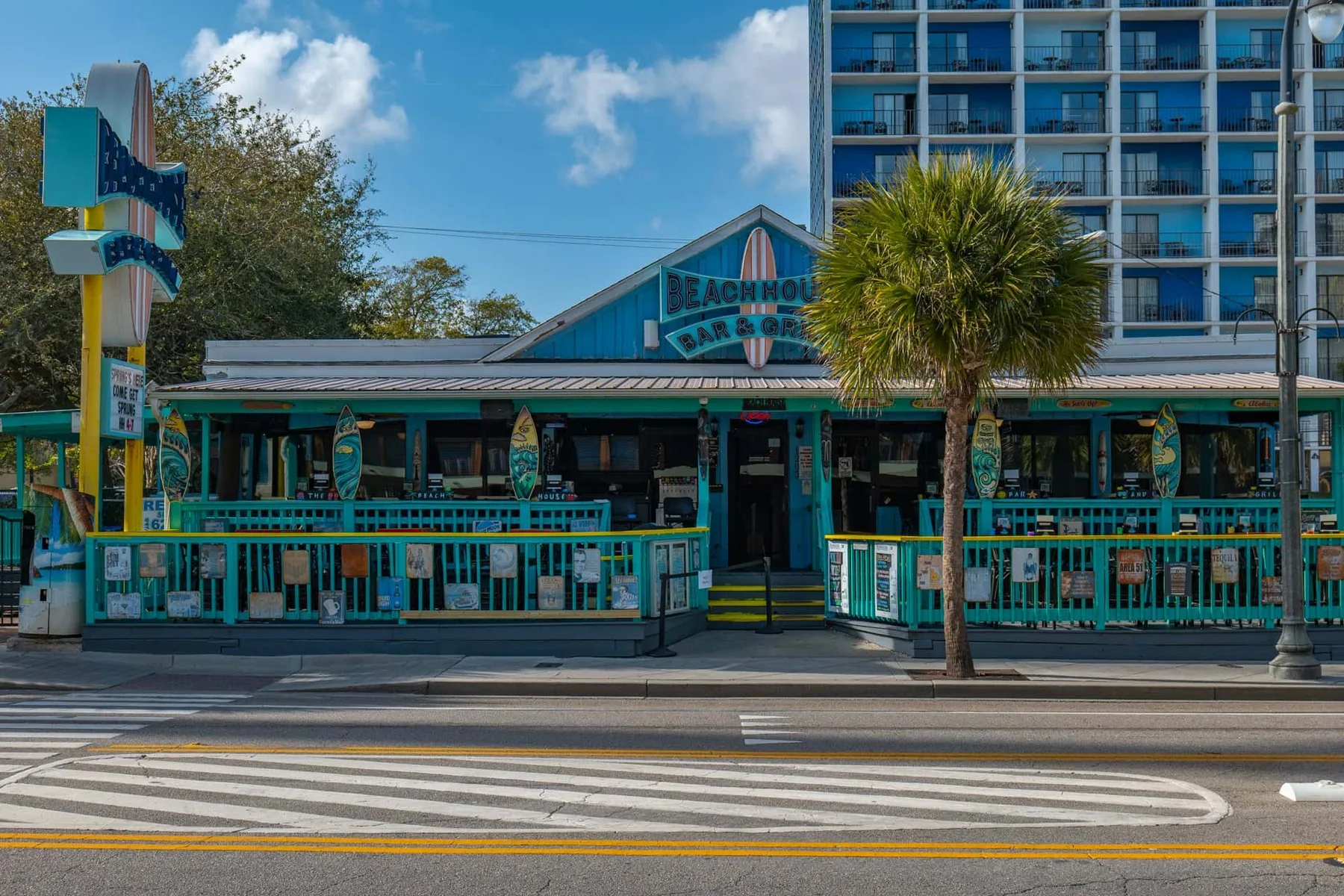 A beachfront restaurant with turquoise railings stands beside a high-rise building.