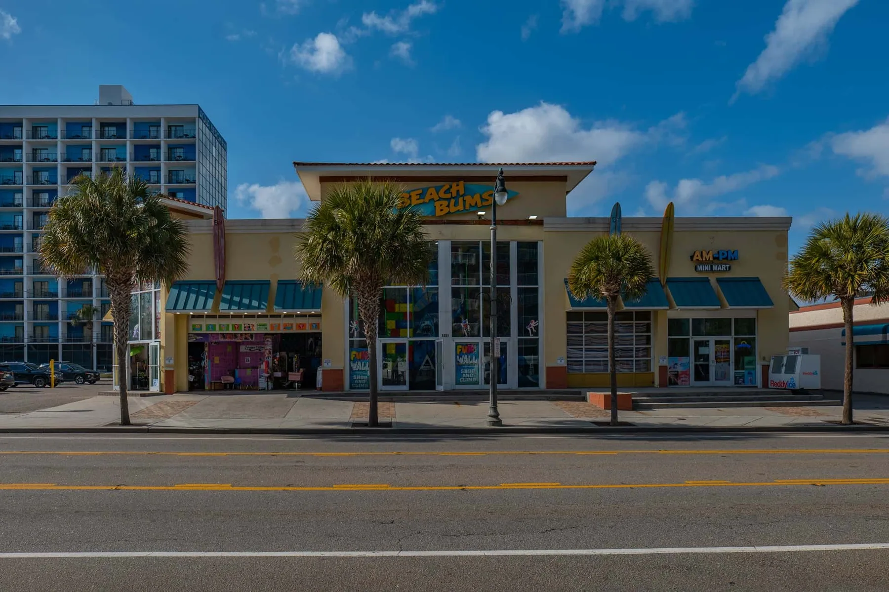 A beachfront retail storefront with glass entrance doors and palm trees along the sidewalk.
