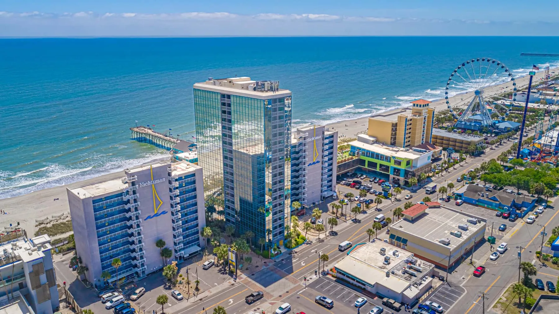 Aerial view of a coastal city with beachfront buildings and a Ferris wheel.