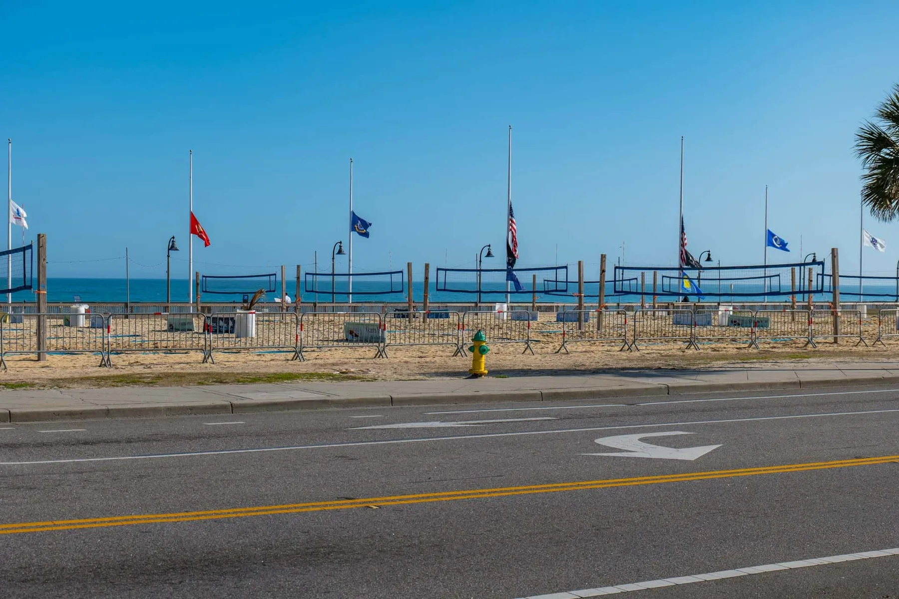 A seaside promenade with volleyball nets and flags beside the road.