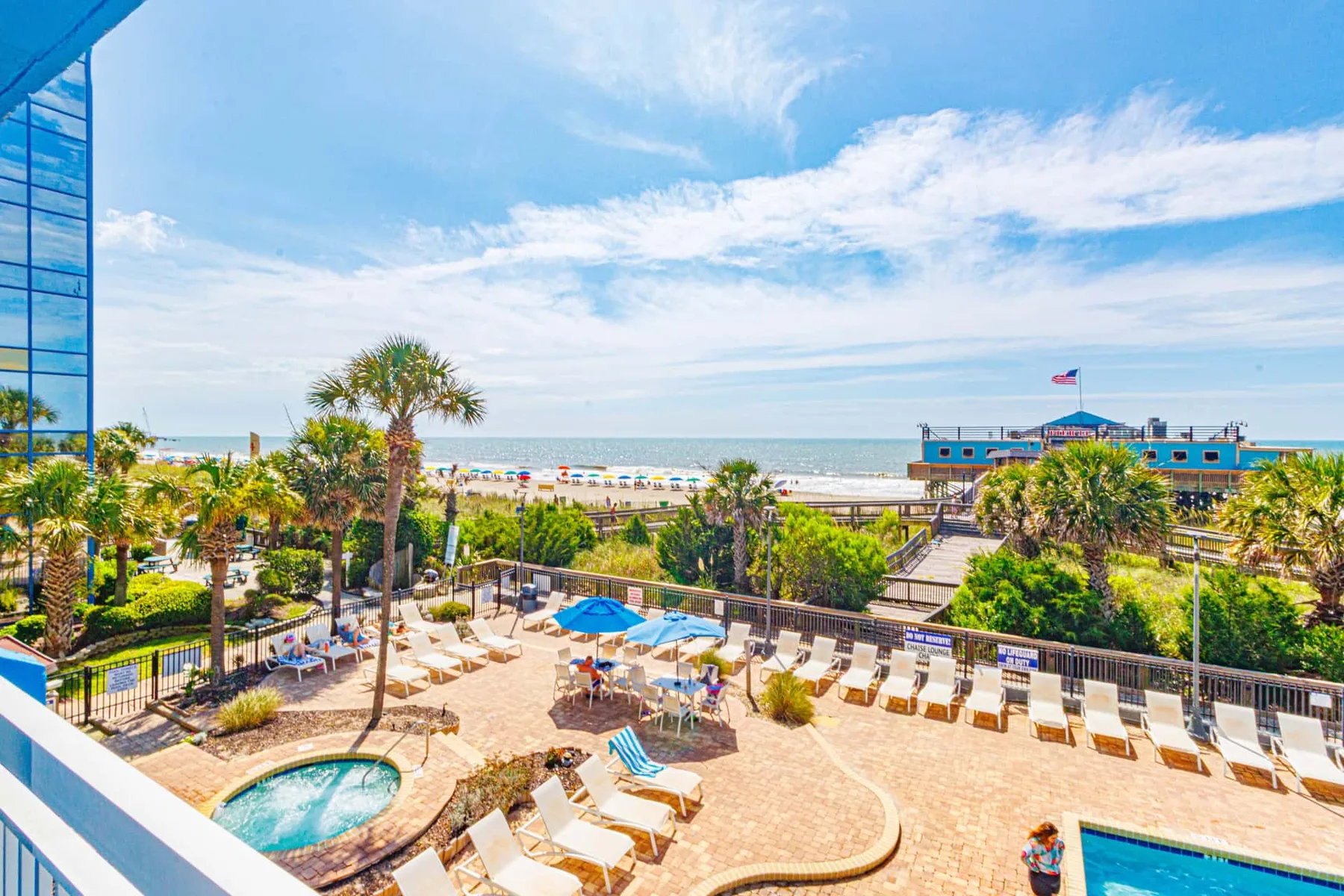 A beachfront pool area with lounge chairs, palm trees, and the ocean beyond.