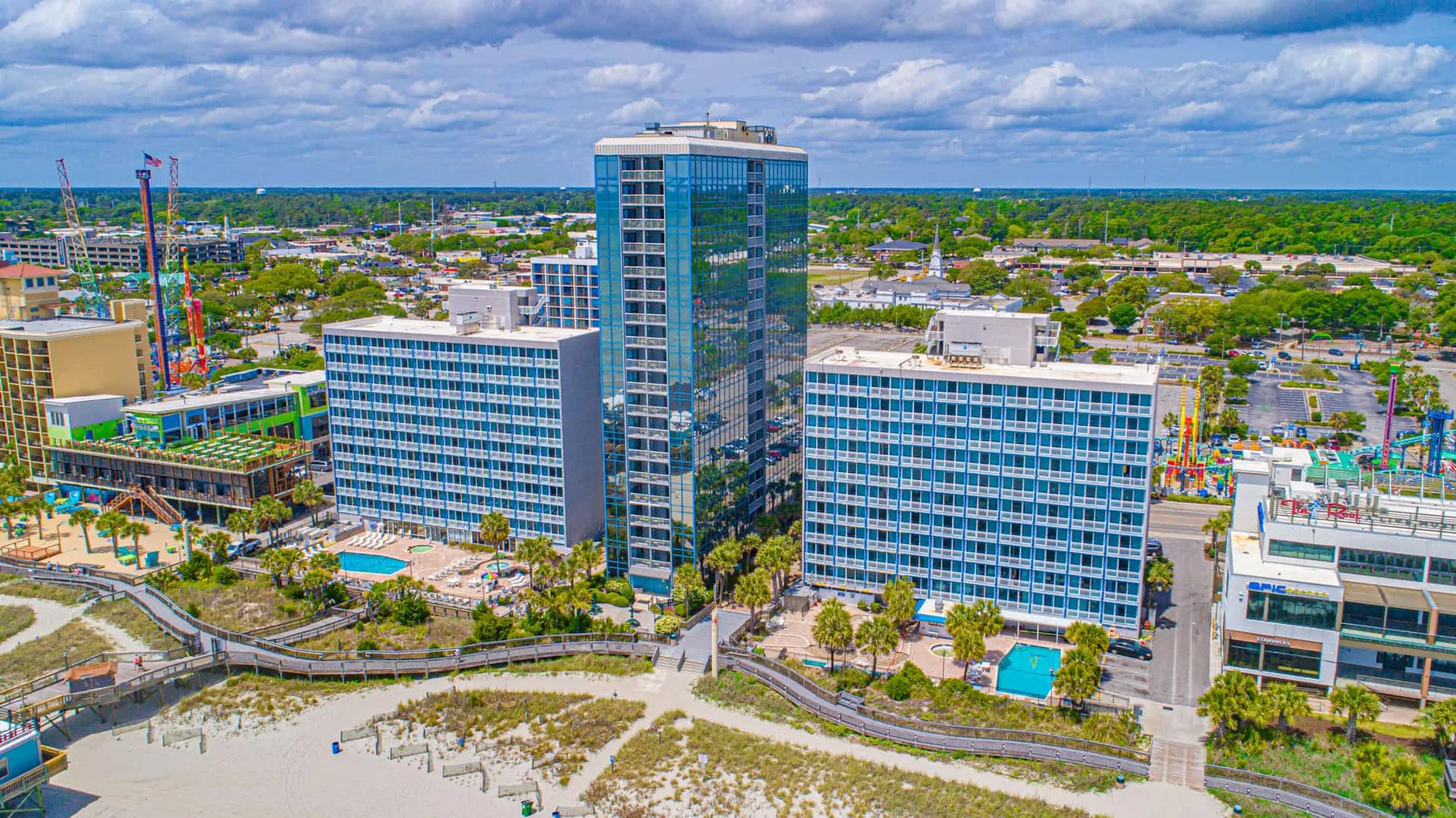 Aerial view of modern waterfront buildings beside a sandy beach and turquoise pools.