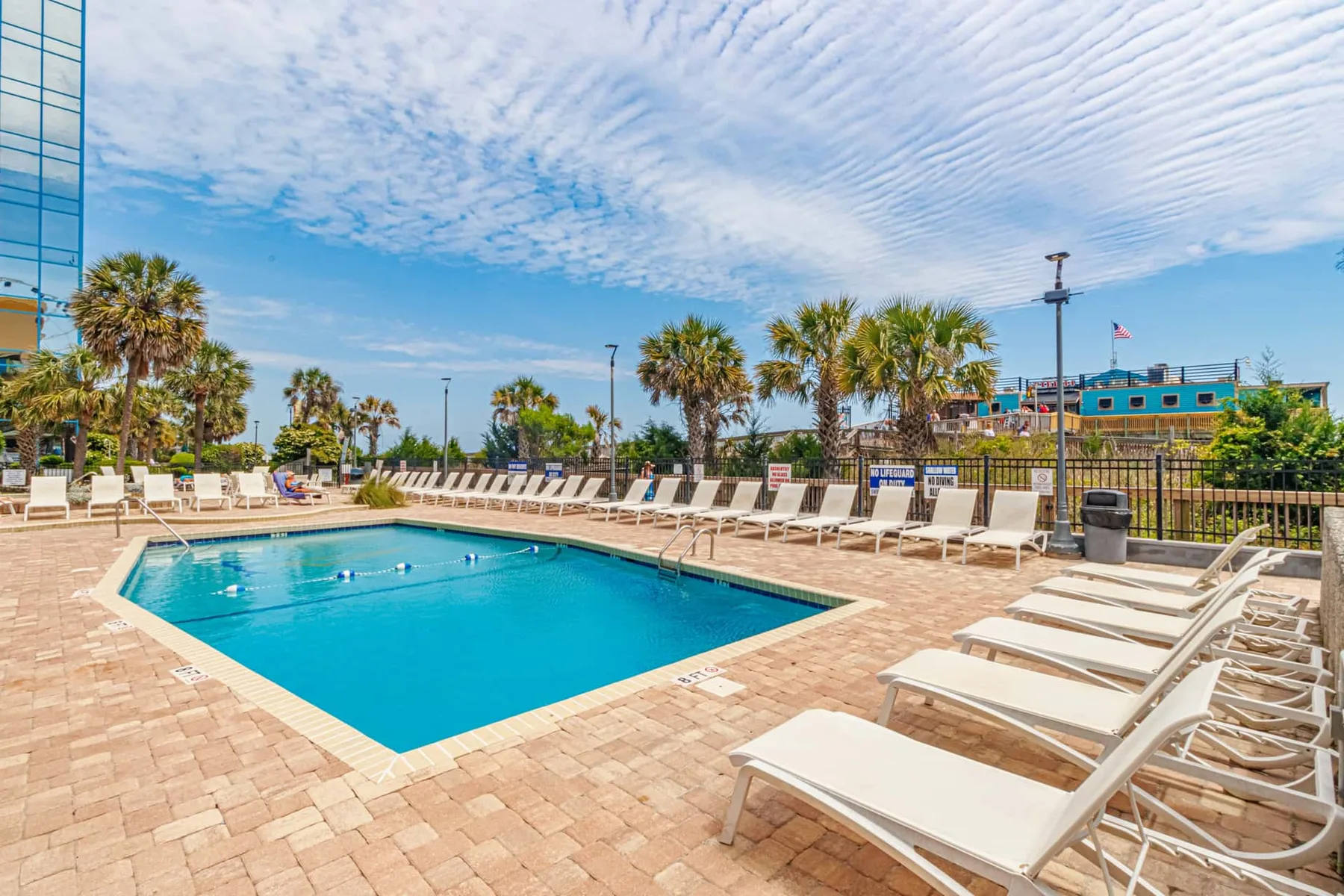 An outdoor swimming pool is surrounded by lounge chairs and palm trees.