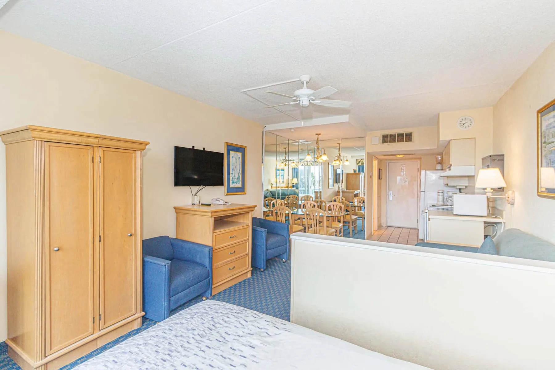 A bright hotel room with a bed, blue seating, and a dining area.