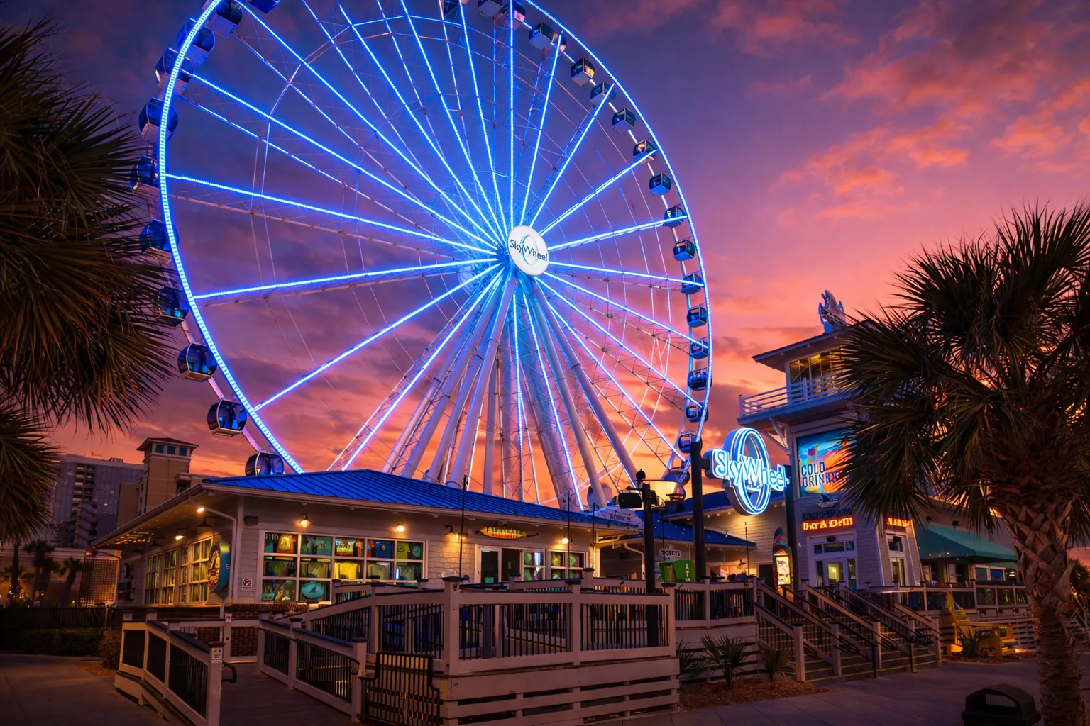 A brightly lit Ferris wheel rises above a boardwalk at sunset.