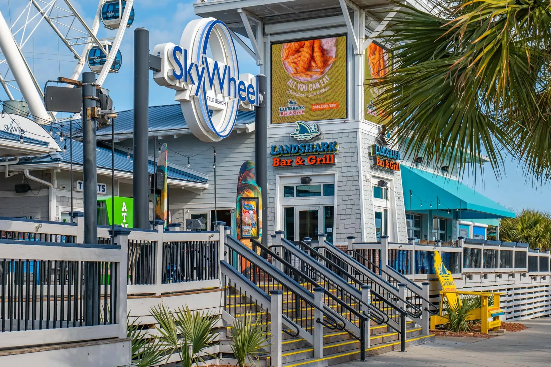 An outdoor restaurant entrance has a raised walkway, railings, and colorful signs.