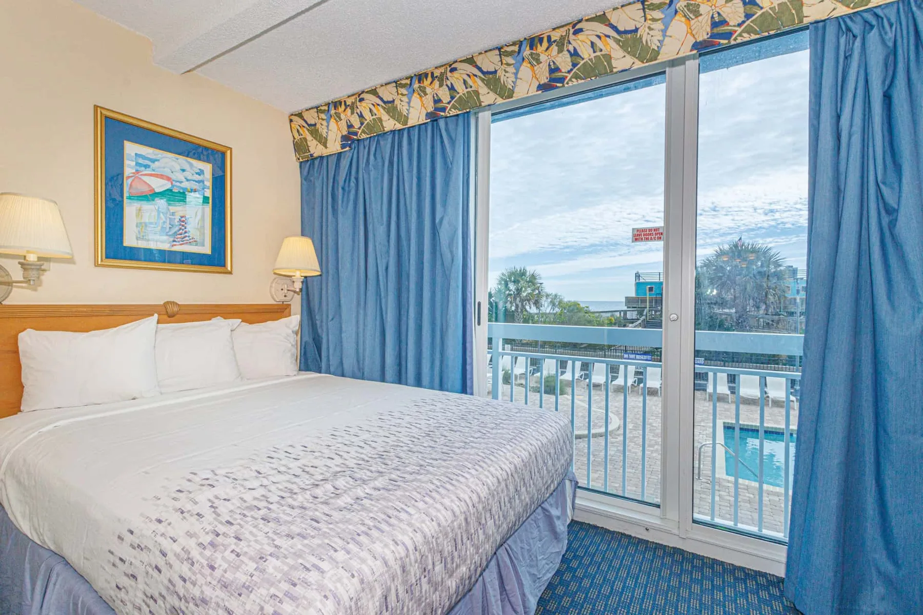 A bedroom with a bed beside blue curtains and a glass balcony door.