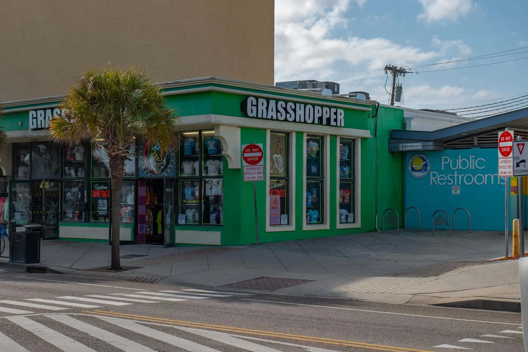 A green storefront stands beside a blue public restroom building on a street corner.