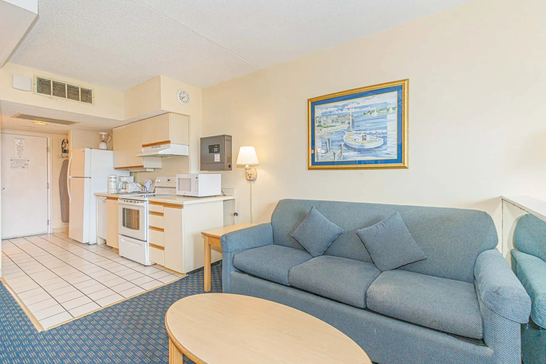 A living area with blue seating beside a compact kitchen and dining table.