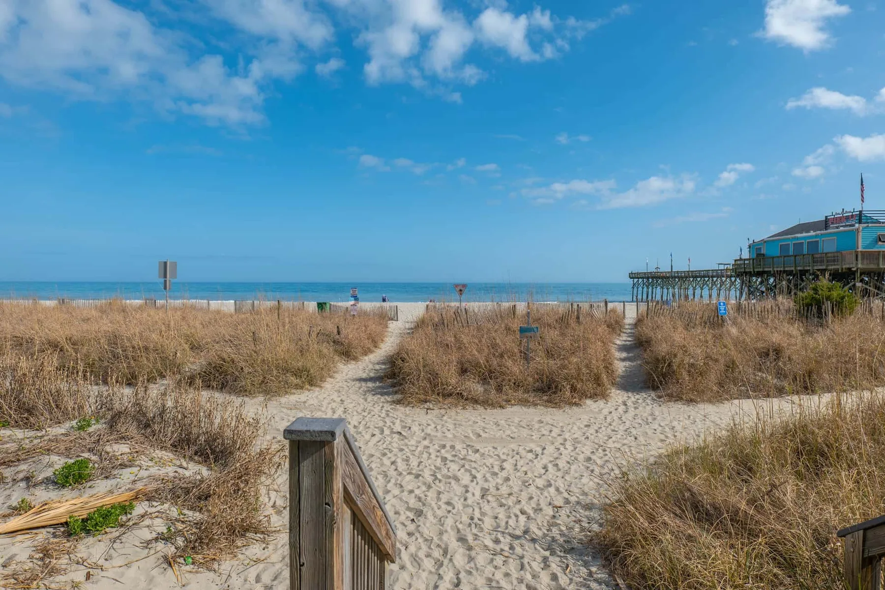 A sandy beach path winds through dune grass toward the ocean.