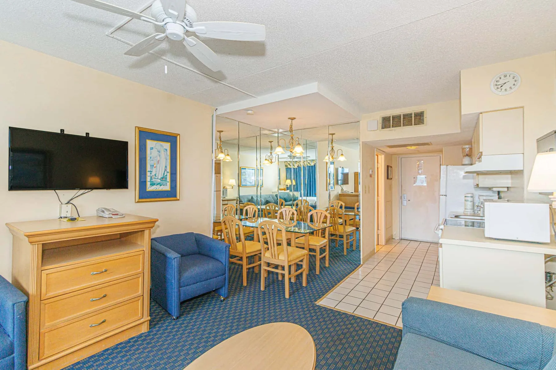 A living and dining area with blue seating, a television, and a wooden dining table.