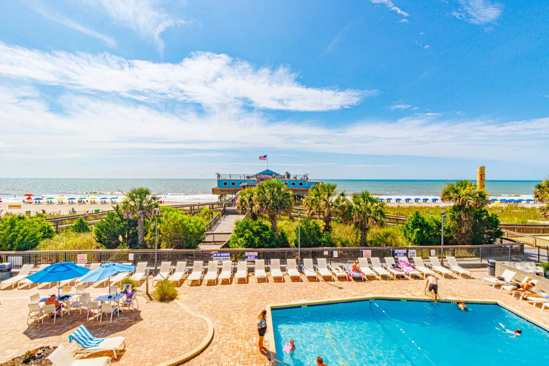 A resort pool and sun loungers overlook the beach and ocean.