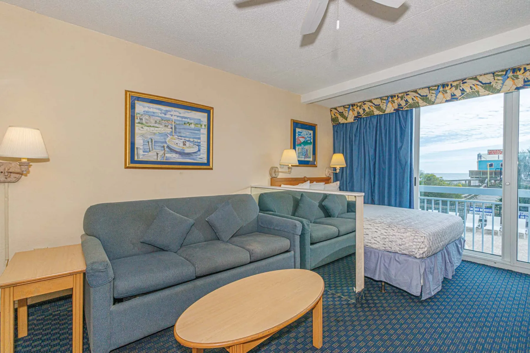 A bedroom sitting area with blue seating beside a bed and balcony doors.