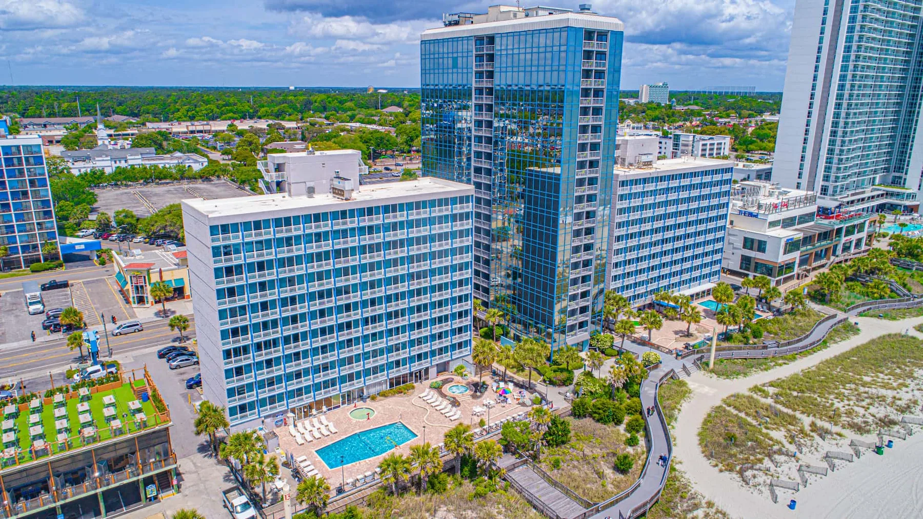 An aerial view of modern glass buildings beside a landscaped beachfront.