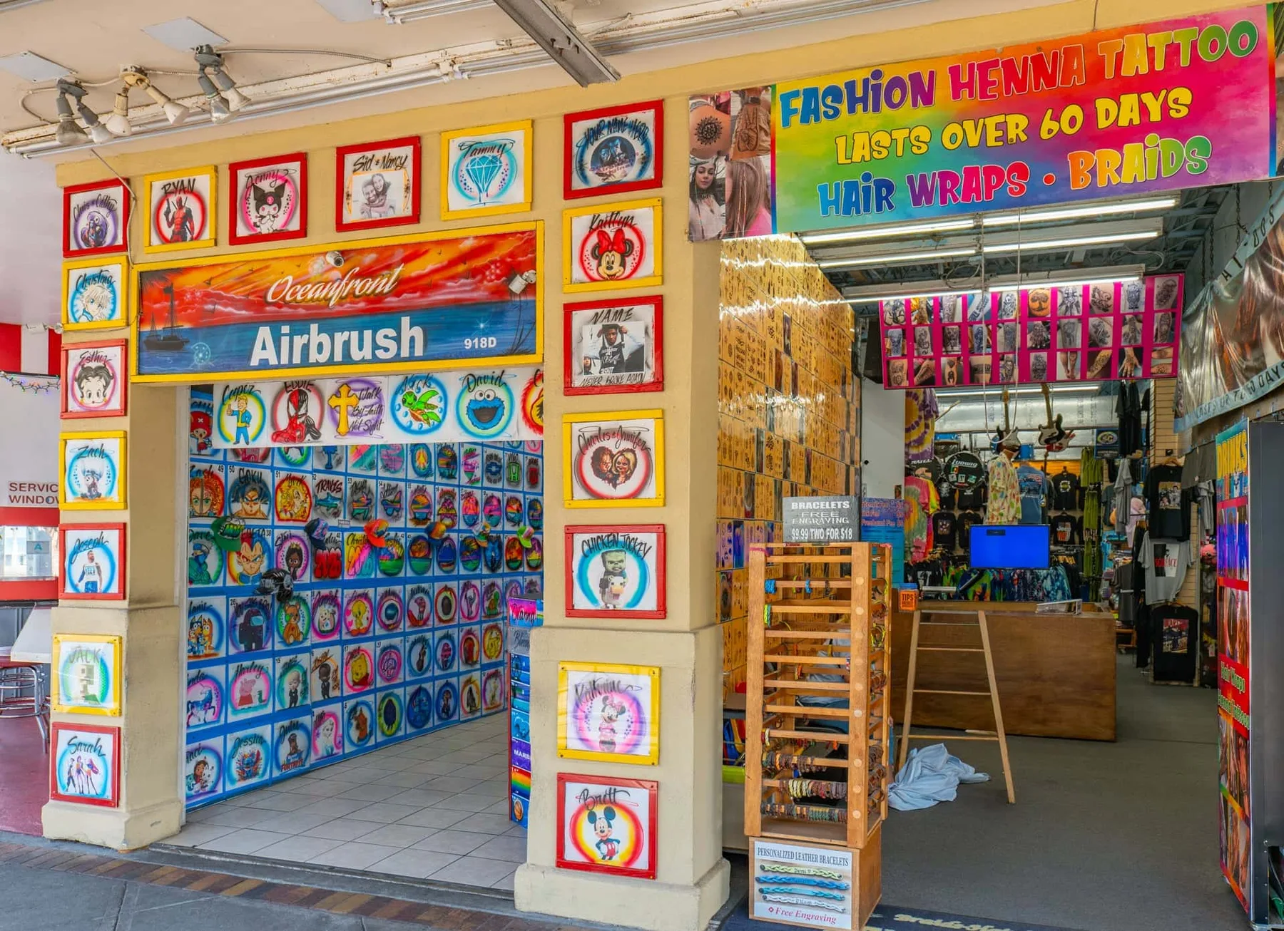 A colorful storefront displays airbrush designs and a sign advertising henna tattoos and hair wraps.