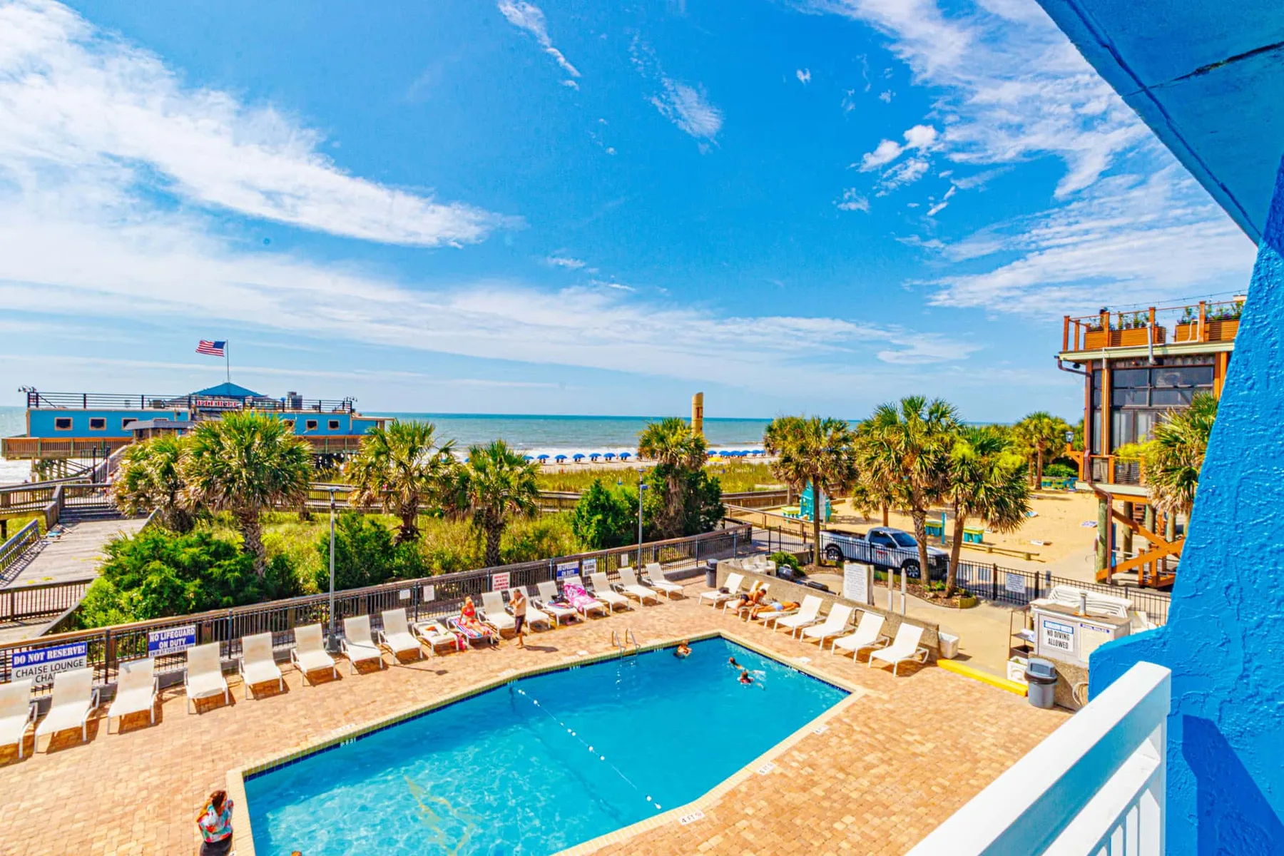 An outdoor swimming pool overlooks a sandy beach and the ocean.