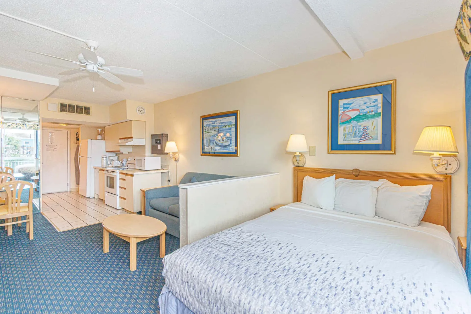 A bedroom with a large bed beside a small kitchen and dining area.