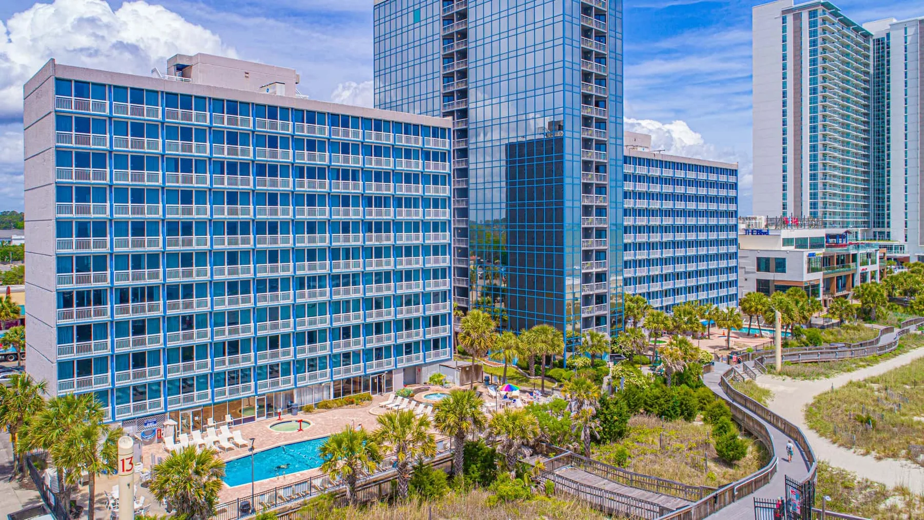 A modern hotel complex overlooks a swimming pool and landscaped grounds.