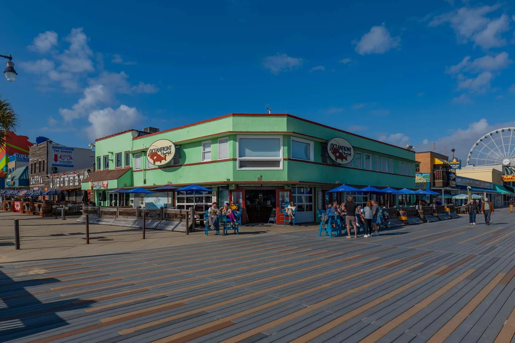 A green corner building with storefronts faces a broad wooden boardwalk.