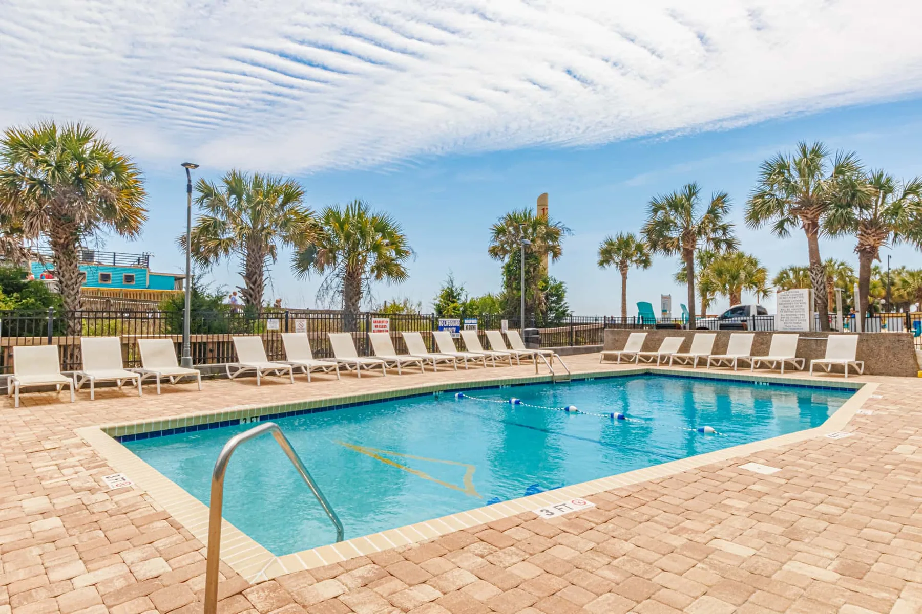 An outdoor swimming pool is surrounded by lounge chairs and palm trees.