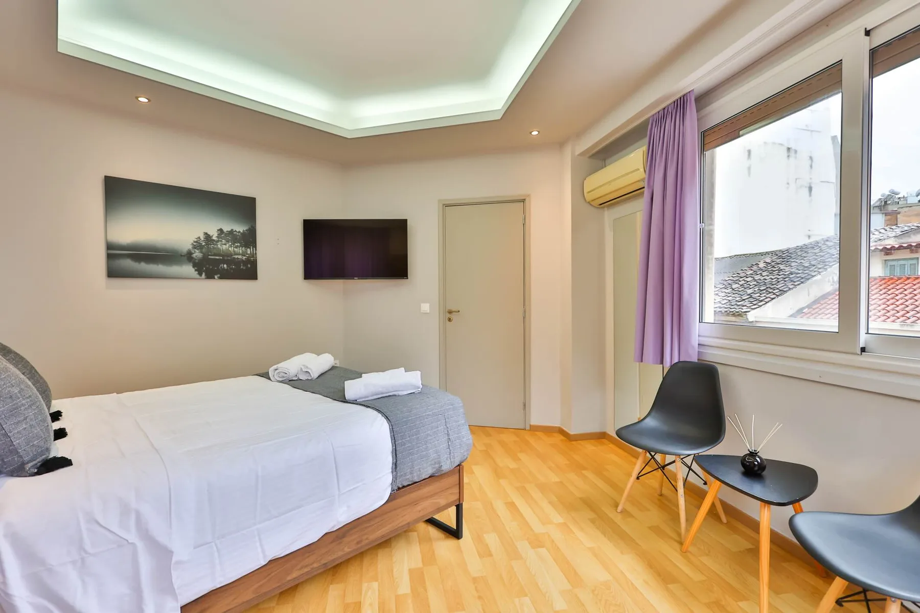 Un dormitorio con una cama, un televisor y asientos junto a una ventana.
