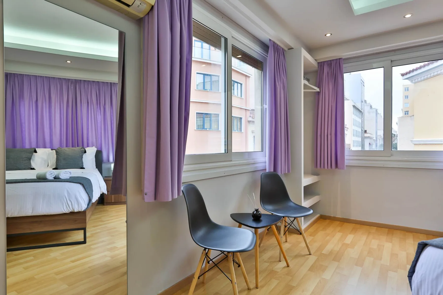 Dormitorio con cortinas moradas, una cama y una pequeña zona de estar junto a las ventanas.