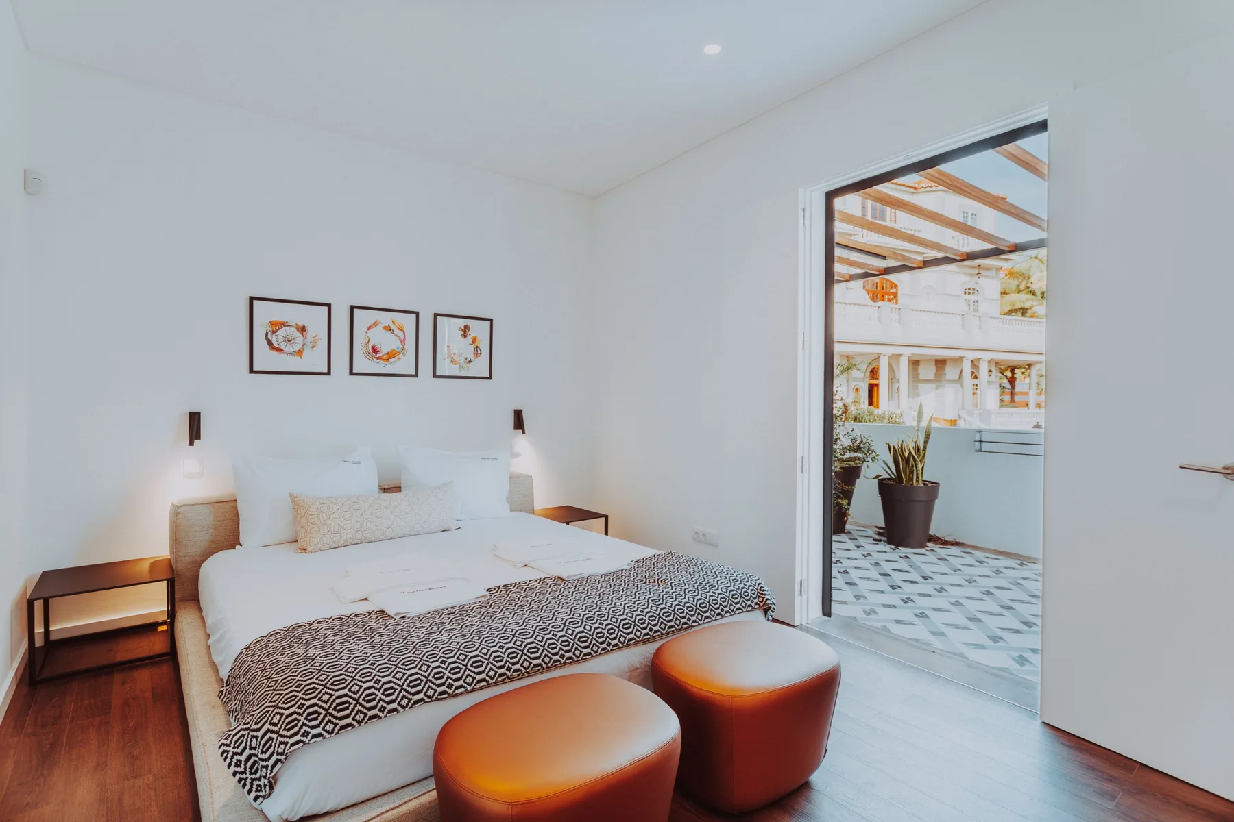 Un dormitorio luminoso con una cama, mesillas y una puerta abierta a una terraza.