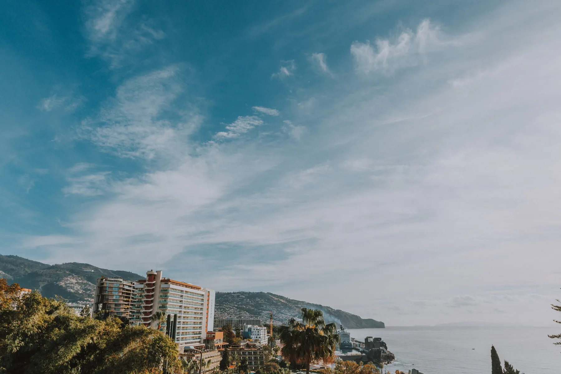 Paisaje costero urbano con edificios, colinas y el mar bajo un cielo nublado.