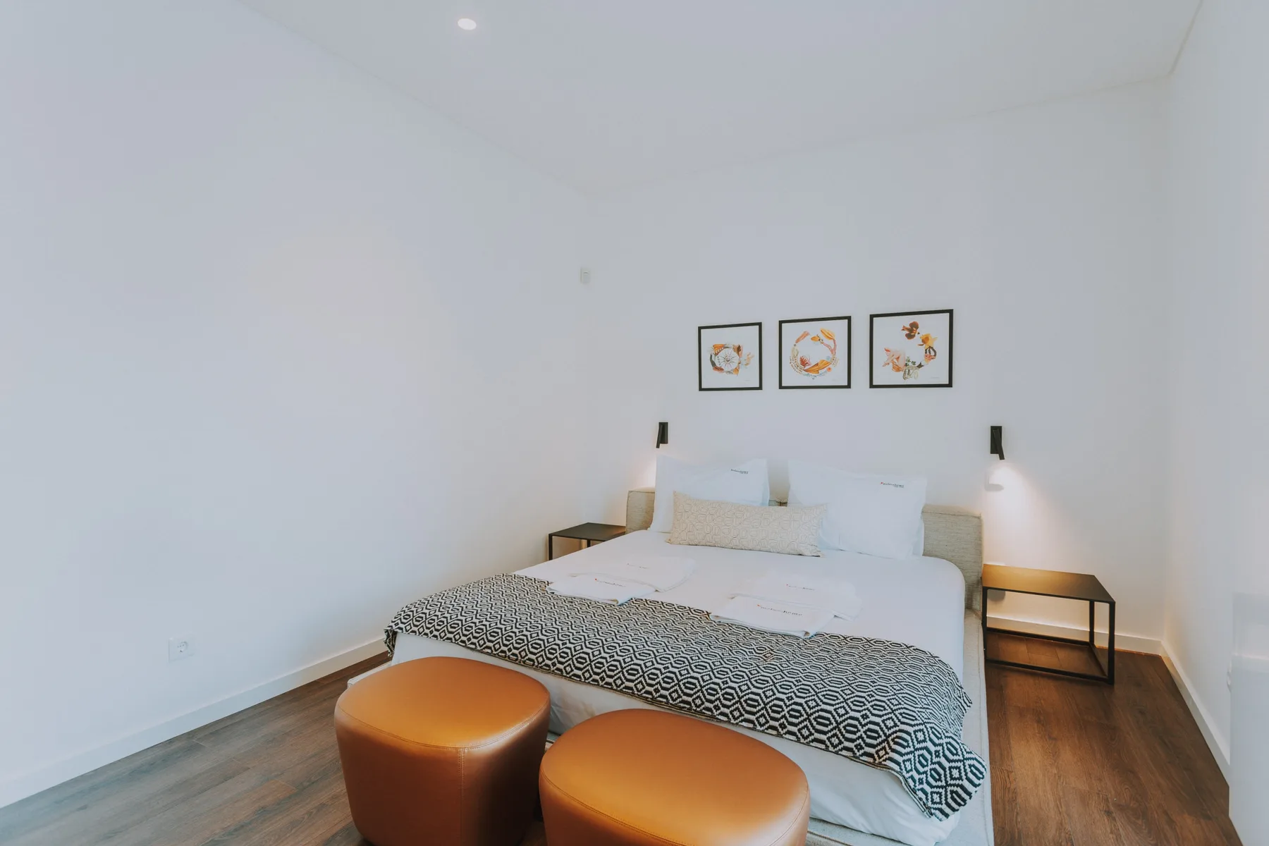 Un dormitorio luminoso con una cama, mesitas de noche y cuadros sobre el cabecero.