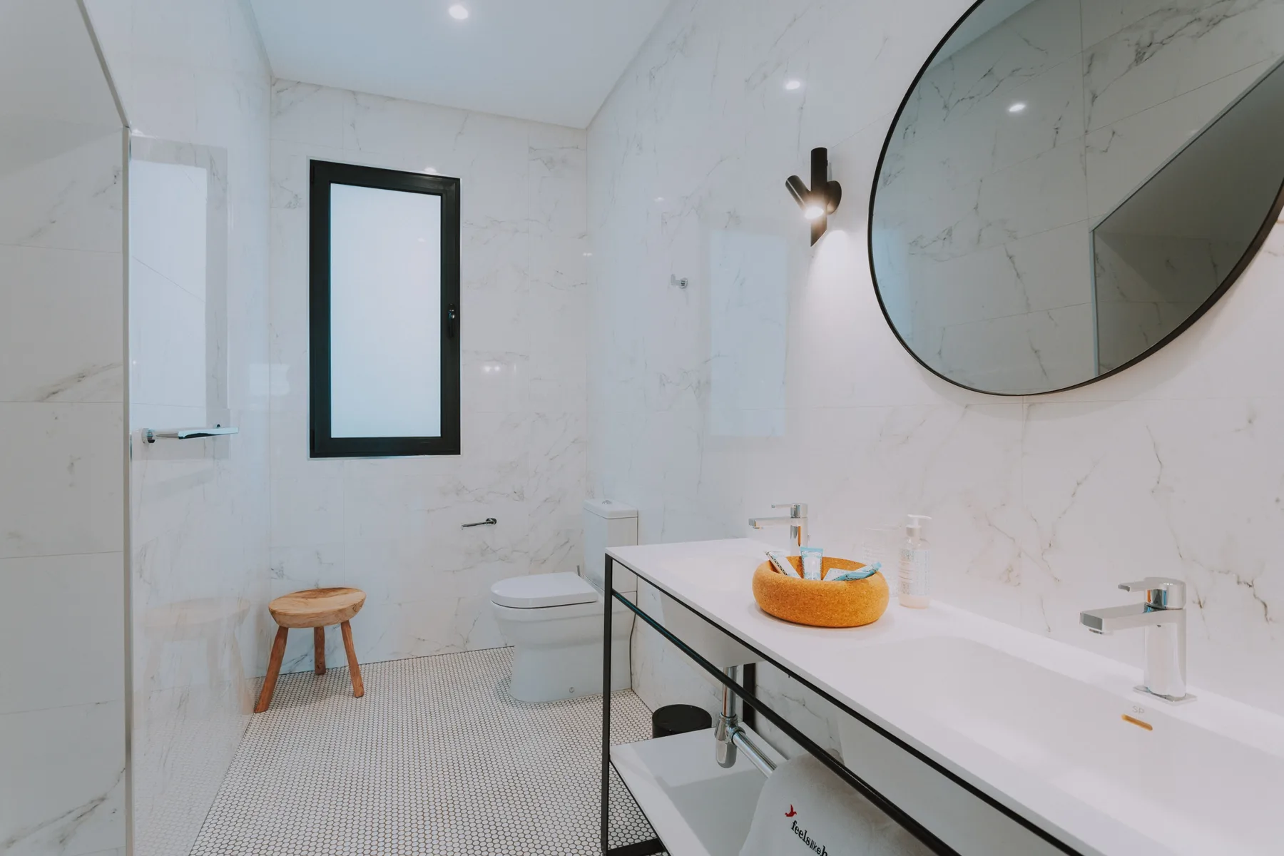 Un baño luminoso con un largo tocador y un gran espejo redondo.