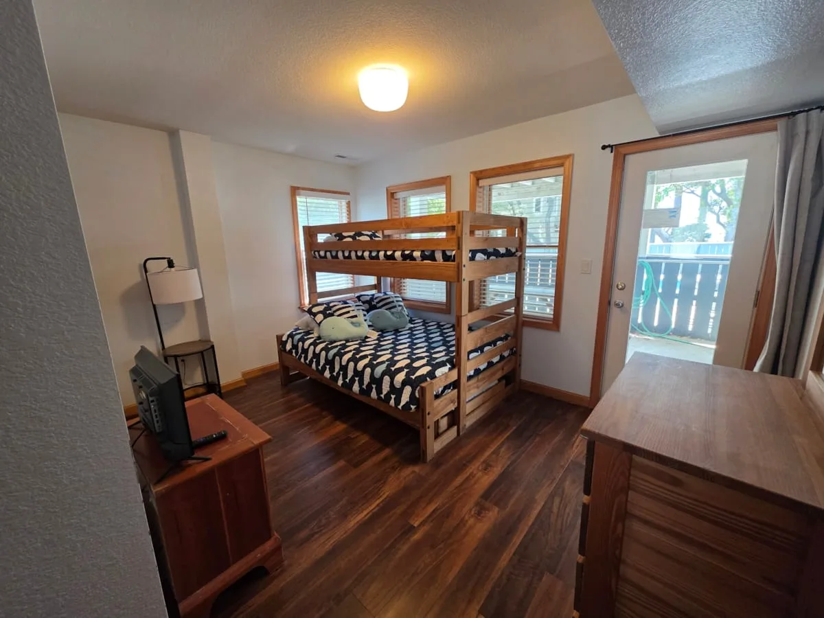 Un dormitorio con una litera de madera, una lámpara y una puerta de vidrio hacia un balcón.