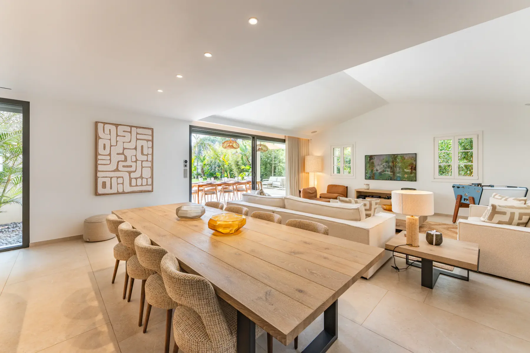 Amplia sala de estar de planta abierta con mesa de comedor de madera, decoración moderna, grandes ventanales y acceso al patio exterior.