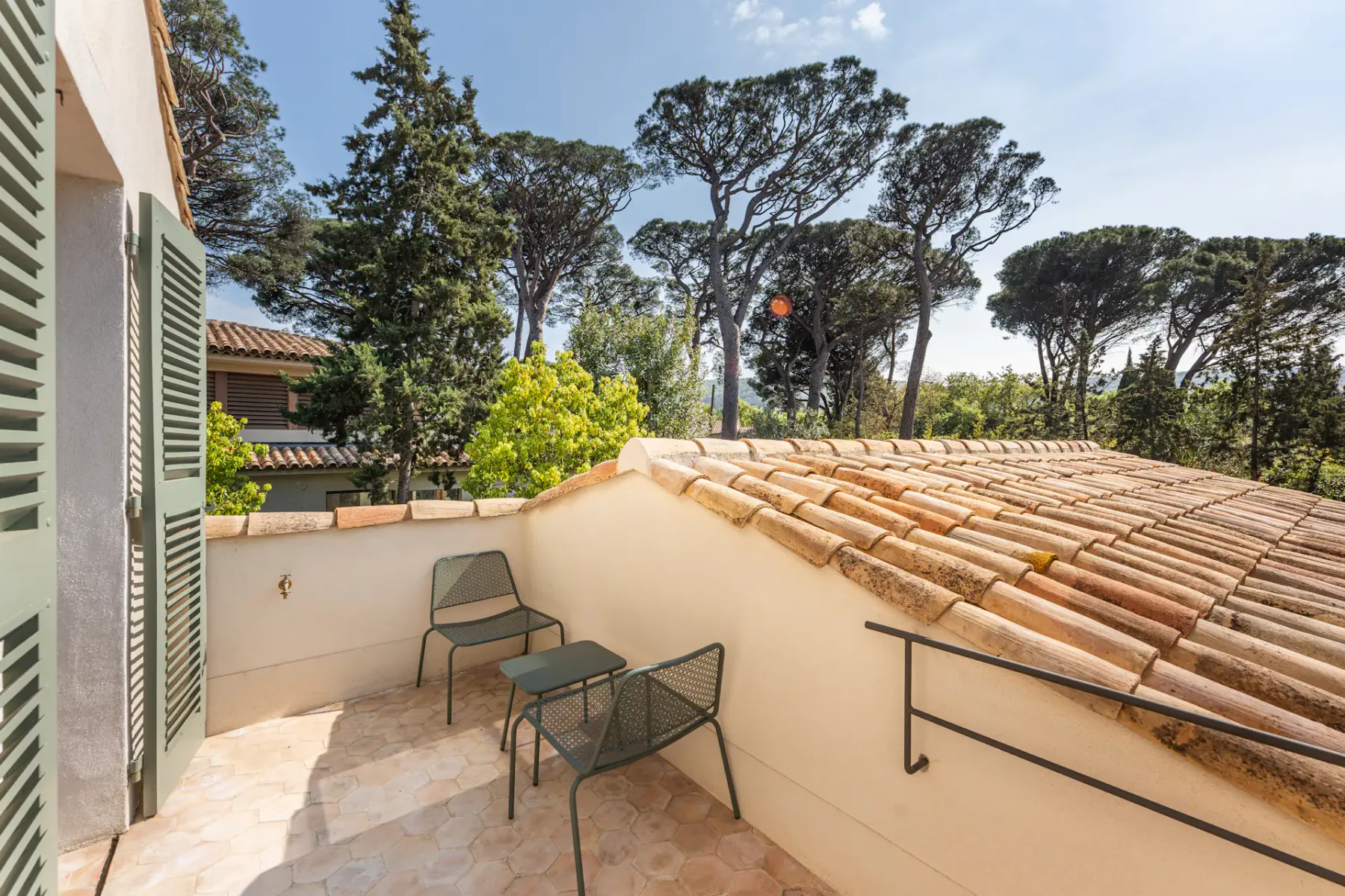 Un balcón soleado con asientos al aire libre ofrece vistas a árboles frondosos y tejados cercanos.