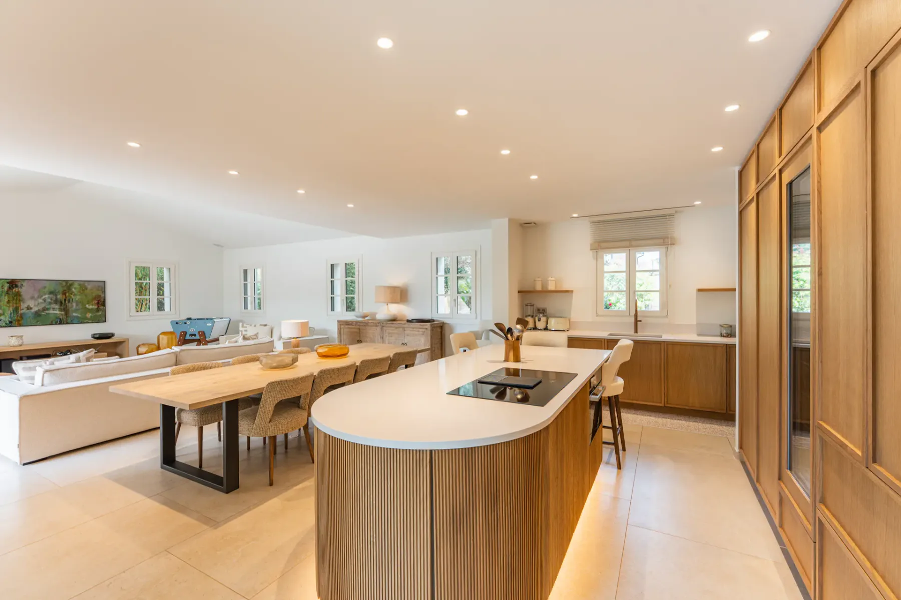 Amplio espacio de planta abierta con cocina y sala de estar, con armarios modernos de madera, una isla central, una mesa de comedor y una acogedora zona de asientos.