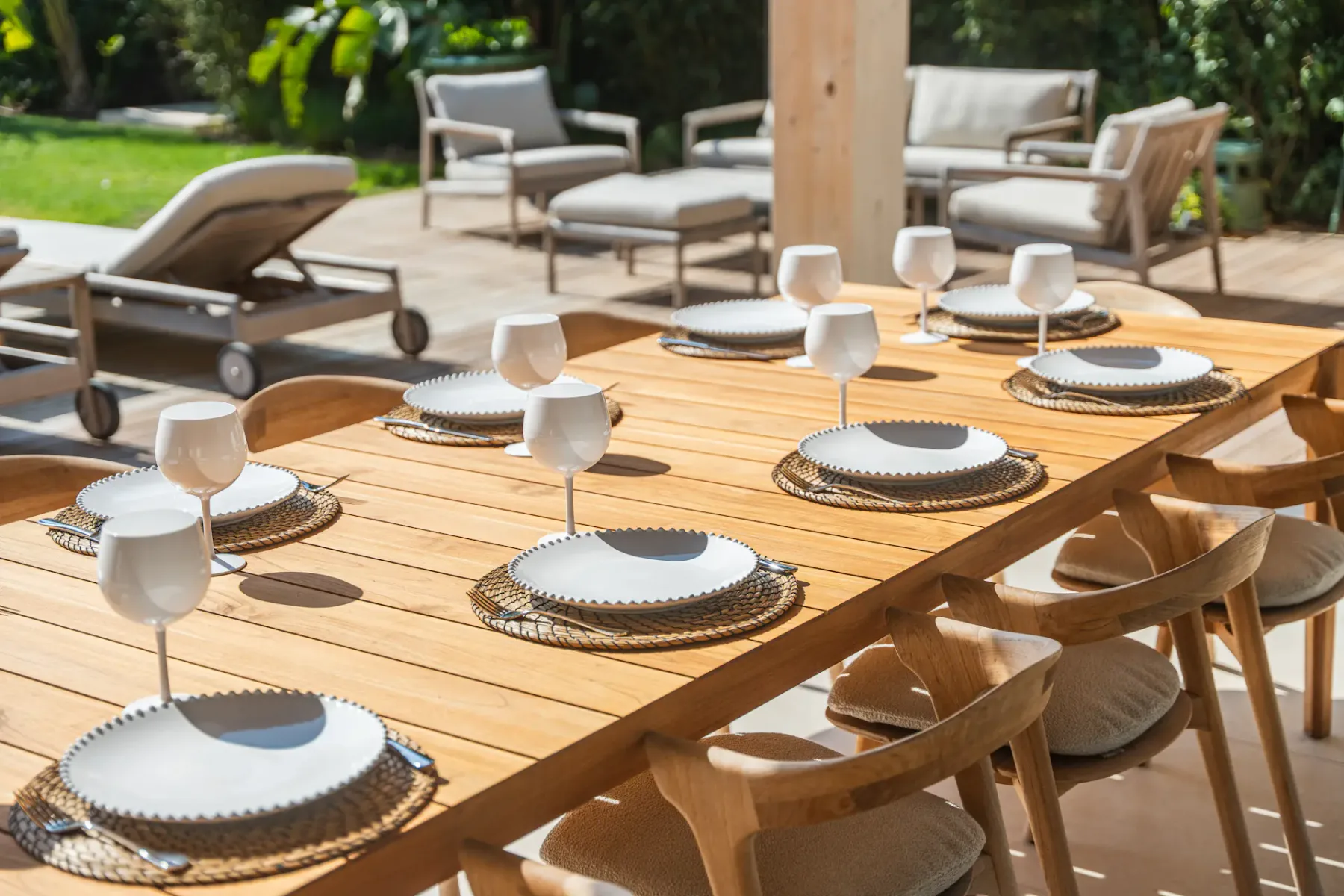 Una zona de comedor exterior con una mesa preparada y asientos con cojines en un patio soleado.