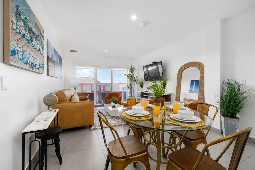 Step into your bright, open living space where natural light pours through floor-to-ceiling windows. Gather around the styled dining table for meals, unwind on the leather sofa, and enjoy modern comforts with thoughtful coastal touches throughout.