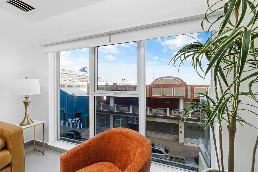 Bright living space with floor-to-ceiling windows, modern furnishings, and an urban cityscape beyond—where natural light and style meet.