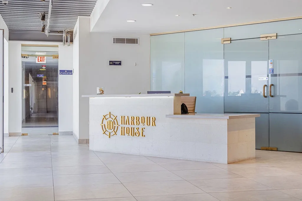 The modern reception area at Harbour House welcomes guests with sleek design, featuring a distinctive nautical logo and bright, airy atmosphere setting the tone for a coastal getaway.