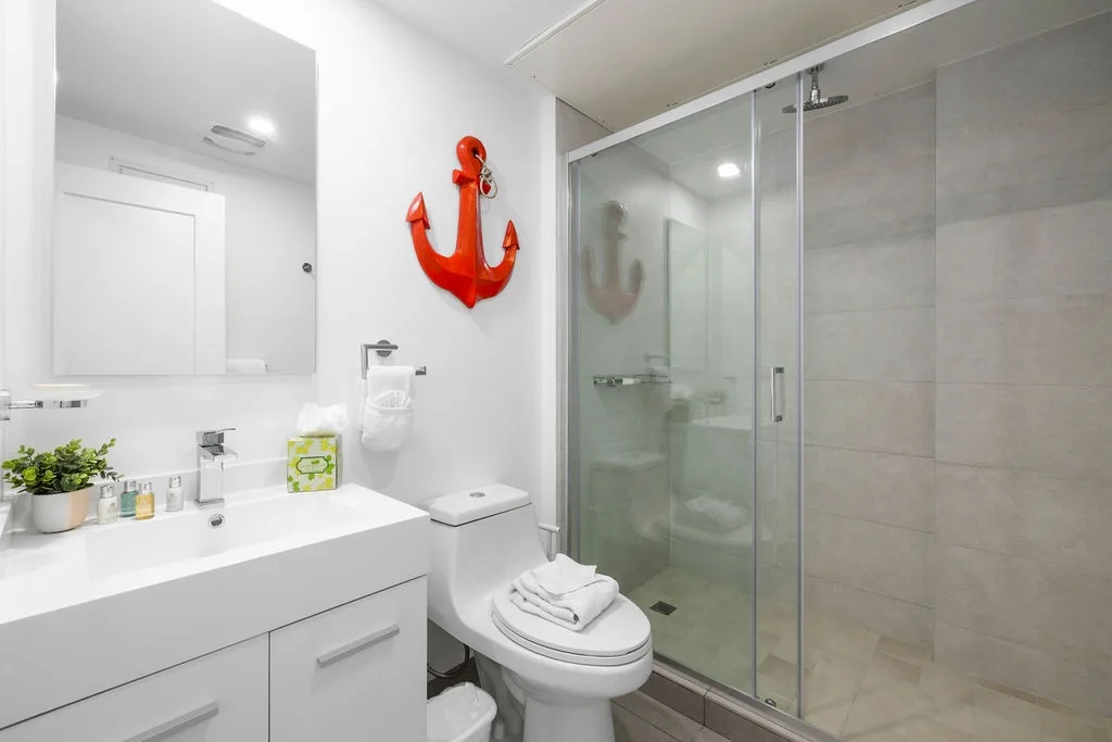 Your private bathroom features a sleek glass-enclosed shower and crisp white vanity, complete with all the essentials and a cheerful coastal touch.