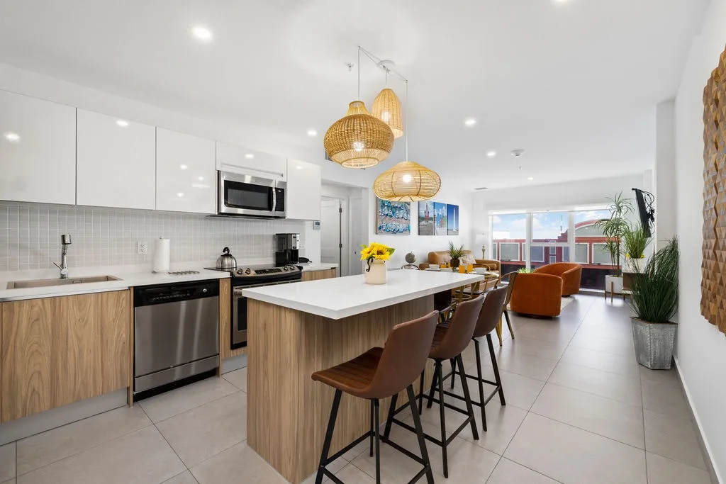 Step into your modern, open-concept haven where sunlight floods the stylish kitchen and living area. Gather around the spacious island for coffee or meals, relax on the cozy seating, and enjoy vibrant pops of art and greenery throughout.