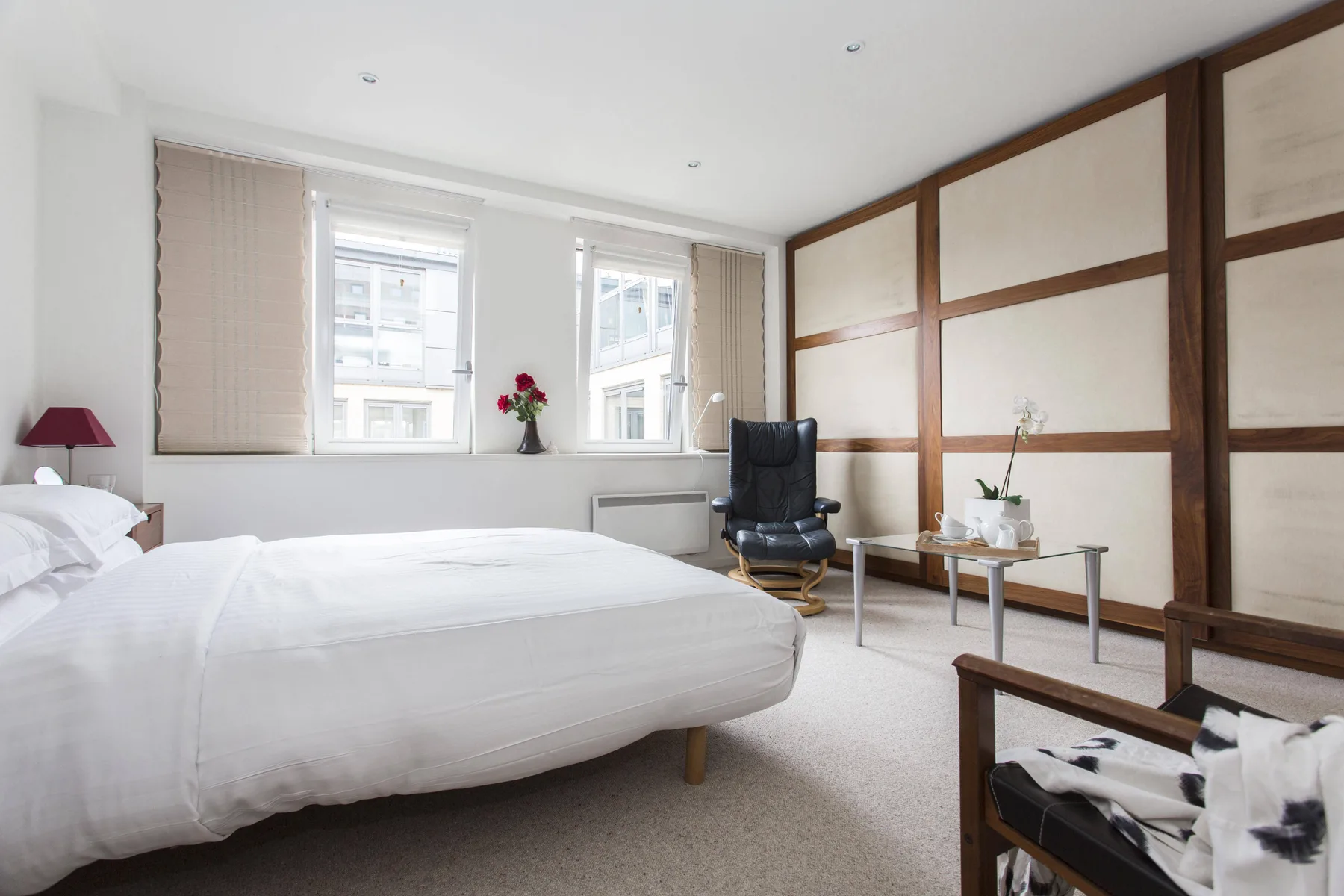 Un dormitorio luminoso con una cama grande, ventanas altas y una zona de estar.